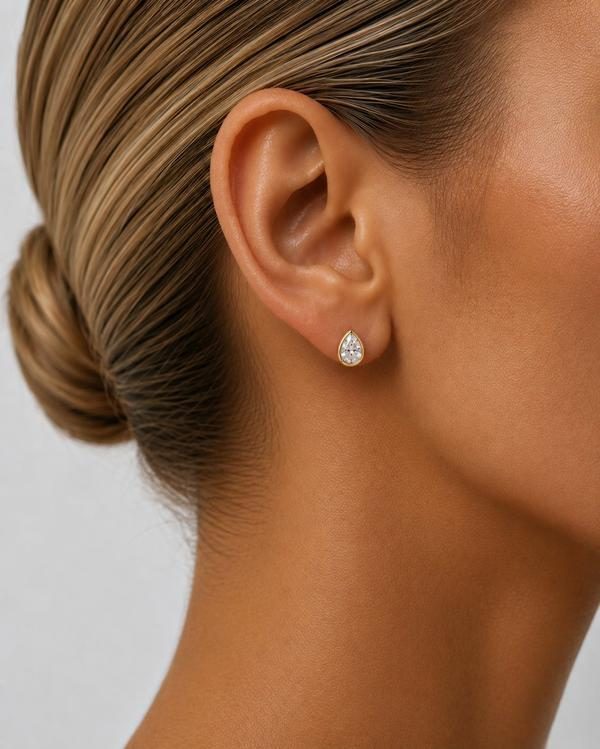 Pear diamond bezel stud in yellow gold, worn on the ear